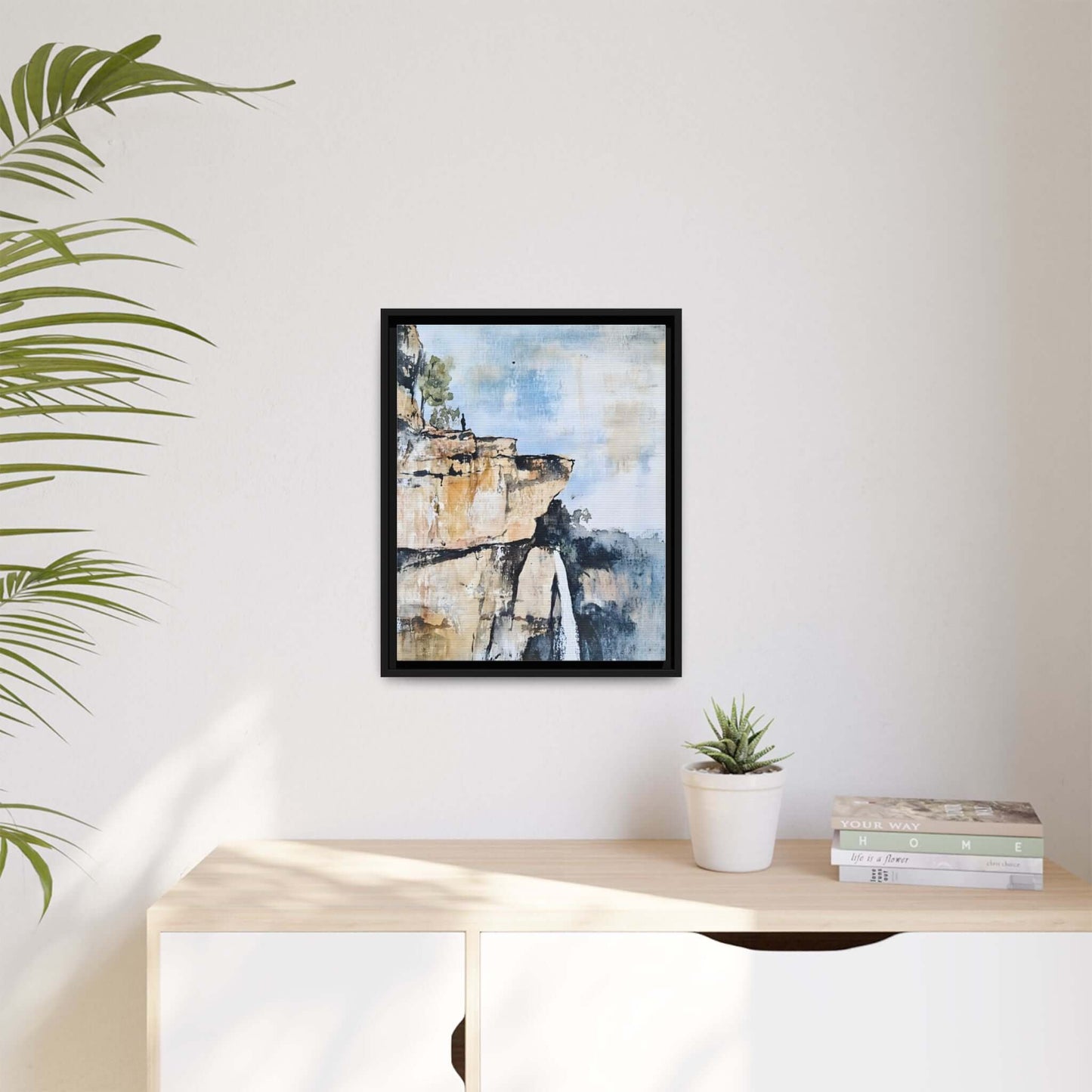 Impressionistic scenic landscape waterfall framed canvas wall art displayed in a minimalist room with plants and books.
