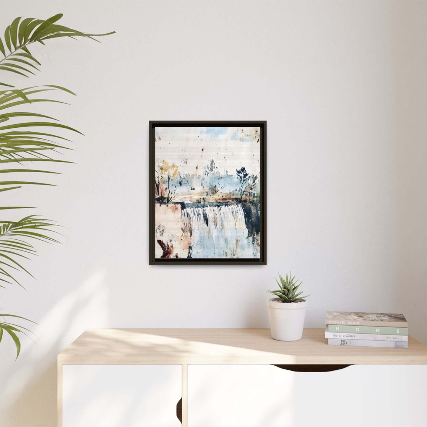 Framed watercolor wall art featuring serene landscape decor, hanging on a white wall above a light wooden console with a plant and books.