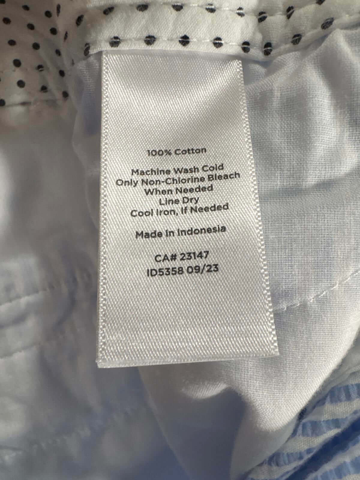 Clothing care label showing washing instructions for 100% cotton fabric, "Machine Wash Cold, Non-Chlorine Bleach, Line Dry."