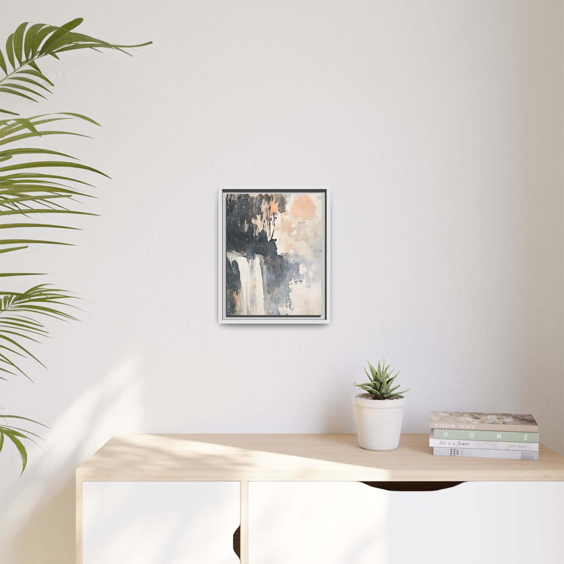Framed waterfall art print on canvas in a modern home interior with plants and books on a light wooden console.