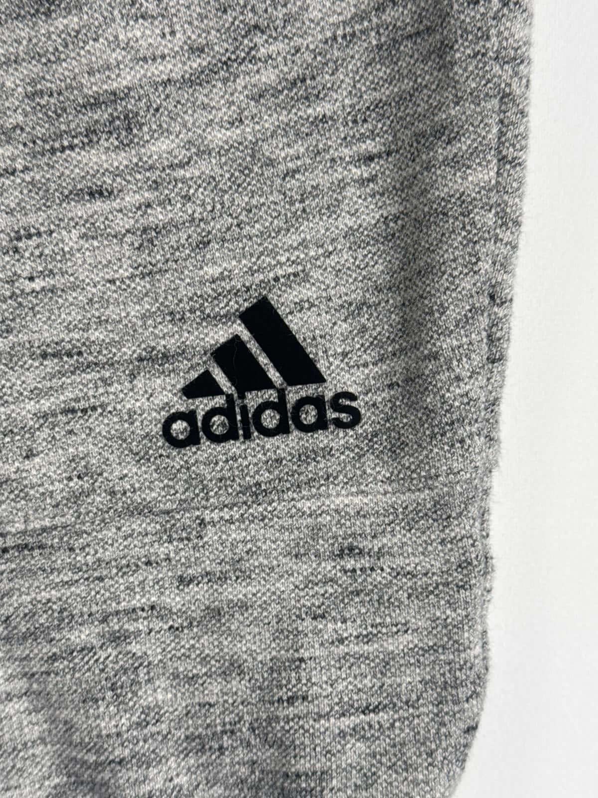 Close-up of Adidas jogger pants with iconic logo on gray fabric, highlighting sporty style.