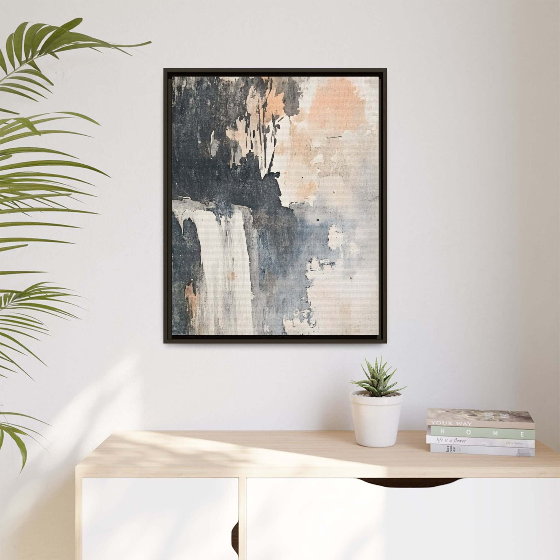 Framed waterfall art print on matte canvas, displayed in a modern home setting with potted plant and books, size options available.
